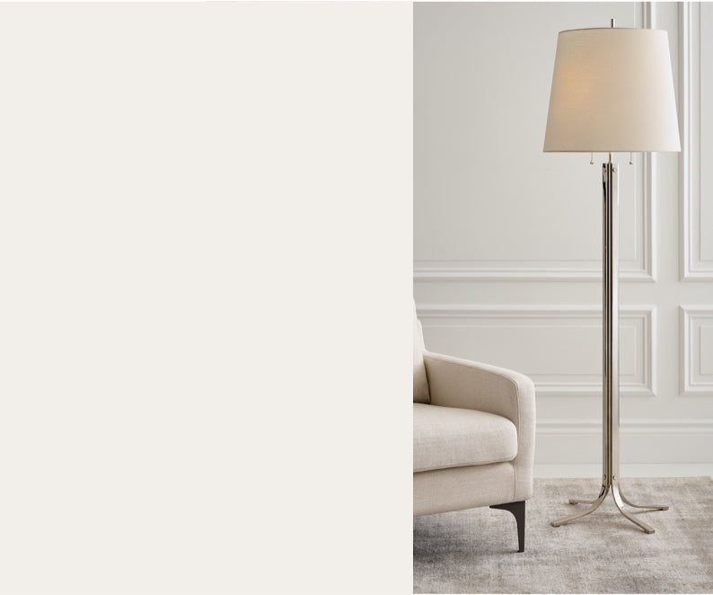 A silver, four-footed lamp next to a beige armchair.